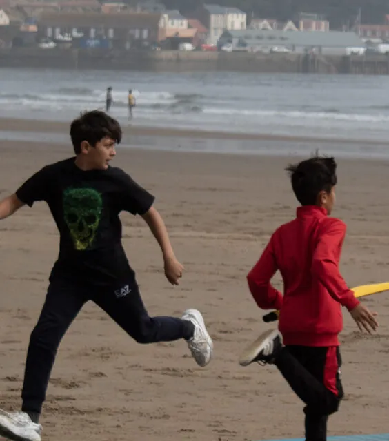 Kids running between the wicket during a beach cricket game.